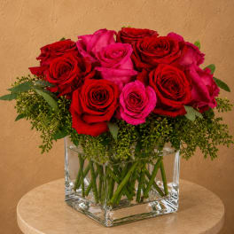 Red and pink roses arranged in a clear glass cube vase