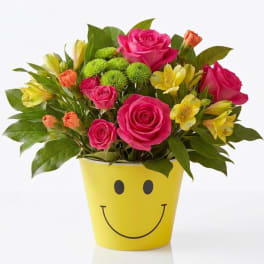 Bouquet of pink roses and yellow flowers in a yellow smiley-face pot
