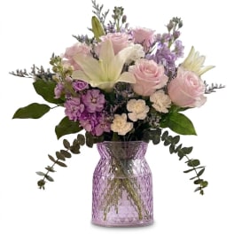 Pink roses and lilies in a purple glass vase with lavender filler