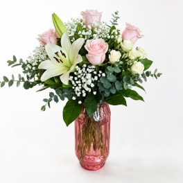 Pink roses and a white lily in a pink glass vase