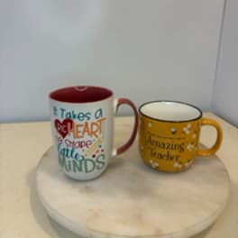 Two printed ceramic mugs on a round tray, one white and one yellow.