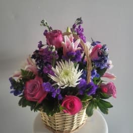 Basket arrangement of pink roses, white lilies, and purple flowers