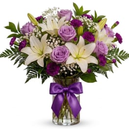 Lavender roses and white lilies in a glass vase with a purple ribbon