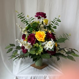 Mixed bouquet of magenta, yellow, and white flowers in a green vase