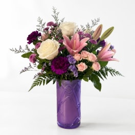 Mixed bouquet of roses, lilies, and purple flowers in a purple vase