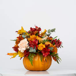 Autumn flower arrangement in a pumpkin-shaped container with red, orange, and cream blooms