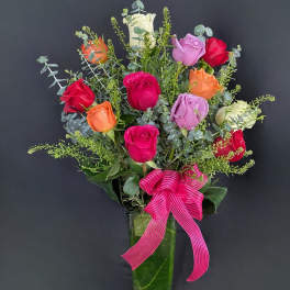 Mixed roses in a tall glass vase with a pink ribbon bow