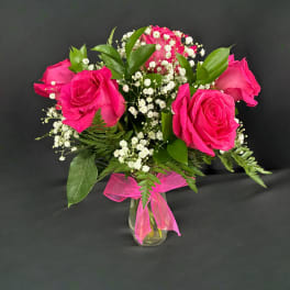 Pink roses with baby's breath in a clear glass vase tied with a pink ribbon