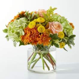 Orange and yellow flowers in a clear glass vase with pale pink roses