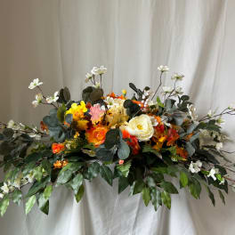 Large floral arrangement with orange, yellow, and white blooms and trailing greenery