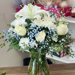 White lilies, roses, and daisies in a glass vase with blue baby's breath