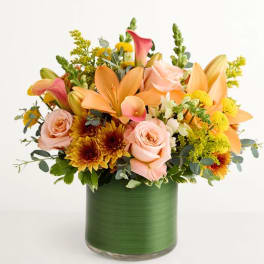 Mixed bouquet of peach lilies, pink roses, and yellow flowers in a green vase