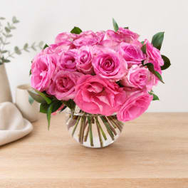 Pink rose bouquet in a clear glass vase on a wooden table