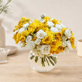 Yellow and white roses arranged in a clear glass bowl vase