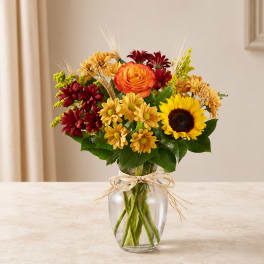 Mixed bouquet with sunflowers, roses, and daisies in a clear glass vase