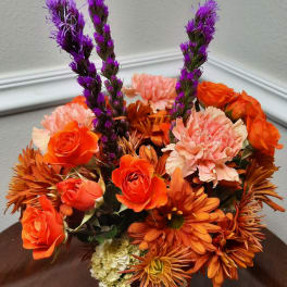 Orange and pink floral arrangement with purple spikes in a vase