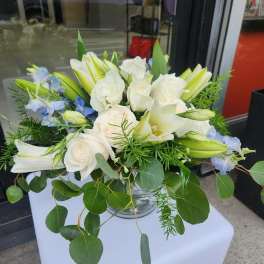 Low arrangement of white roses and lilies with light blue flowers in a clear glass bowl vase