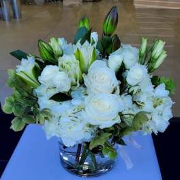 Low glass vase of white roses, lilies, and hydrangeas in a rounded arrangement