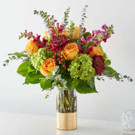Bouquet of orange roses, green hydrangeas, and burgundy blooms in a glass vase