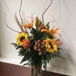Orange lilies and sunflowers arranged in a clear glass vase