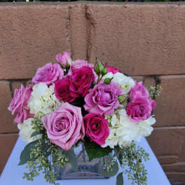 Low arrangement of pink roses and white hydrangeas in a clear glass cube vase