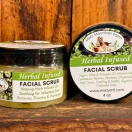 Two jars of herbal infused facial scrub on a wooden surface.