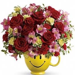 Red roses and pink flowers in a yellow smiley-face mug