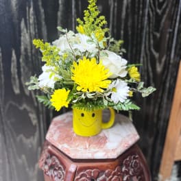 Yellow and white flowers arranged in a smiley-face mug