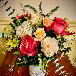 Mixed red and cream roses with peach blooms and trailing eucalyptus in a painted white vase