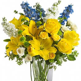 Yellow roses and lilies with blue and white flowers in a clear vase