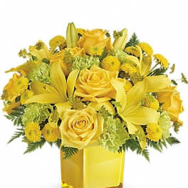 Yellow roses and lilies arranged in a square glass vase