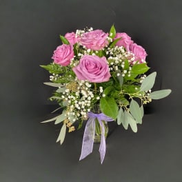 Pink rose bouquet in a glass vase with white filler flowers and a purple ribbon