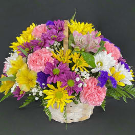 Mixed bouquet of yellow, purple, pink, and white flowers in a woven basket