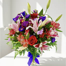 Mixed bouquet of lilies, roses, and purple flowers in a glass vase