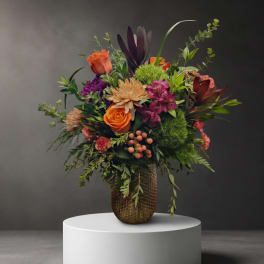 Mixed bouquet of orange, purple, and pink flowers in a textured vase