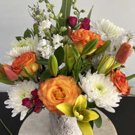 Mixed bouquet of orange roses, white chrysanthemums, and yellow lilies in a textured vase