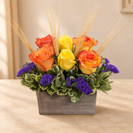 Orange and yellow roses in a gray rectangular planter with purple accents