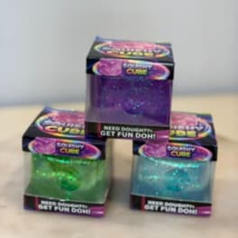 Three glittery dough cubes in colorful boxes stacked on a table