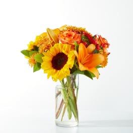 Bouquet of sunflowers, orange lilies, and roses in a clear glass vase