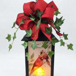 Black lantern with a red bow and ivy, featuring a lit cardinal memorial panel.