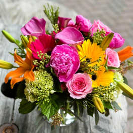 Mixed bouquet with pink, yellow, and orange flowers in a glass vase