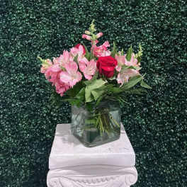 Pink flowers and a red rose in a glass vase beneath a gold "Always Beautiful" sign