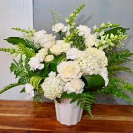 White floral arrangement in a white vase with green foliage