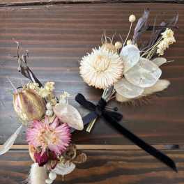 Two small dried floral boutonnieres with ribbon ties on a wooden surface