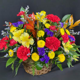Colorful mixed flower basket with red carnations, yellow mums, and purple filler flowers