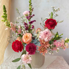 Mixed bouquet of roses, carnations, and snapdragons in a white vase