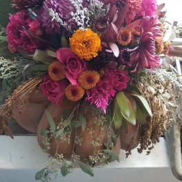 Autumn arrangement of pink roses and mixed orange and purple blooms arranged in a pumpkin container