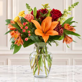 Mixed bouquet with orange lilies, red roses, and yellow blooms in a glass vase
