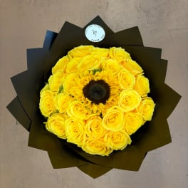 Yellow rose bouquet with a sunflower center wrapped in dark paper