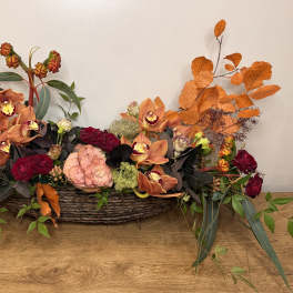 Low floral centerpiece in a woven basket with orange orchids and red roses
